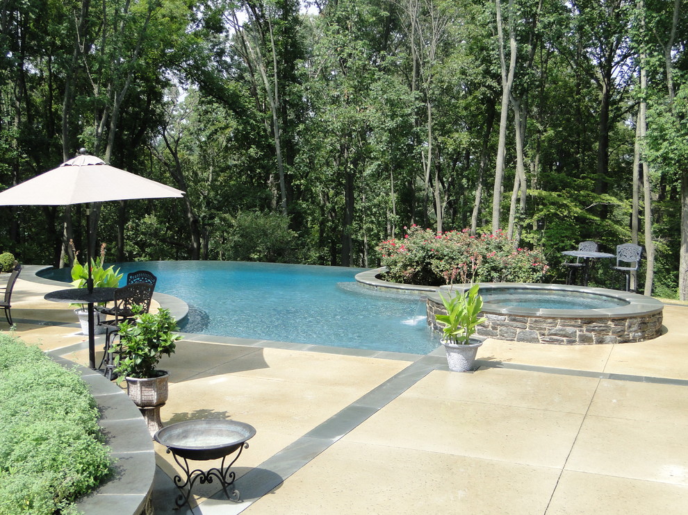Ispirazione per una grande piscina a sfioro infinito design personalizzata dietro casa con fontane e lastre di cemento