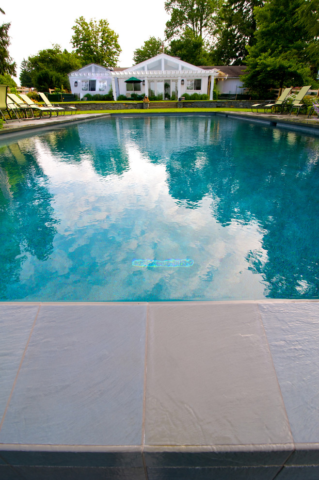 Diseño de piscina con fuente infinita tradicional grande rectangular en patio trasero con adoquines de piedra natural