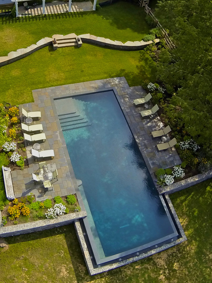 Esempio di una grande piscina a sfioro infinito tradizionale rettangolare dietro casa con fontane e pavimentazioni in pietra naturale