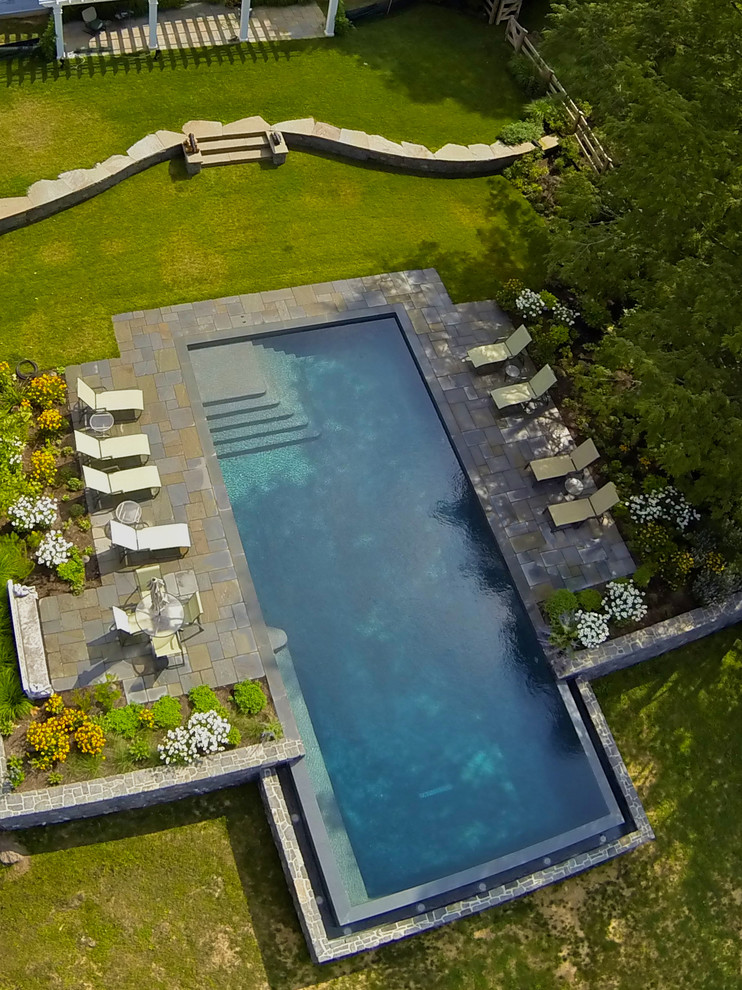 Photo of a large classic back rectangular infinity swimming pool in Wilmington with a water feature and natural stone paving.