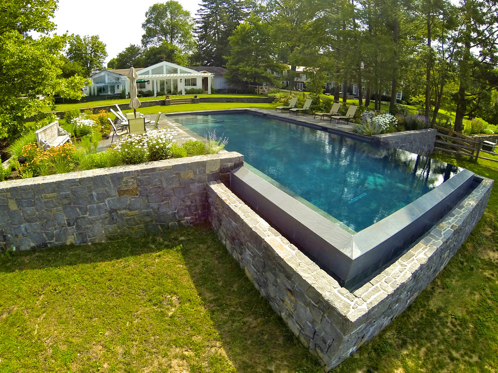 Foto de piscina con fuente infinita clásica grande rectangular en patio trasero con adoquines de piedra natural