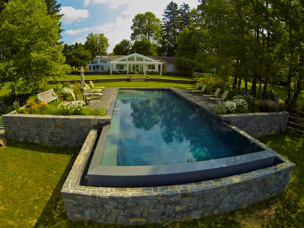 Modelo de piscina con fuente infinita tradicional grande rectangular en patio trasero con adoquines de piedra natural