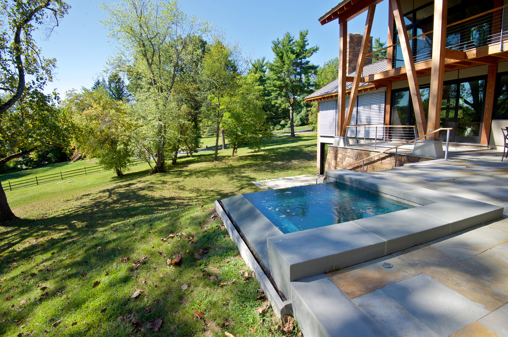 Réalisation d'une petite piscine à débordement et arrière design rectangle avec un bain bouillonnant et des pavés en pierre naturelle.