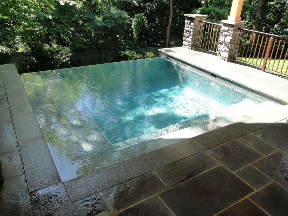 Réalisation d'une petite piscine à débordement et arrière tradition rectangle avec un bain bouillonnant et des pavés en pierre naturelle.