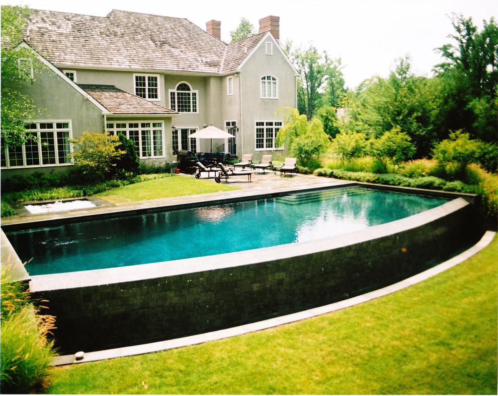 Foto di una grande piscina a sfioro infinito tradizionale personalizzata dietro casa con pavimentazioni in pietra naturale e una vasca idromassaggio