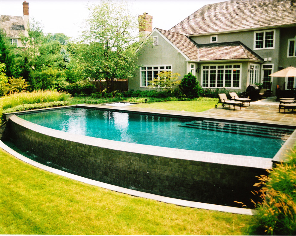 Ispirazione per una grande piscina a sfioro infinito classica personalizzata dietro casa con pavimentazioni in pietra naturale e una vasca idromassaggio