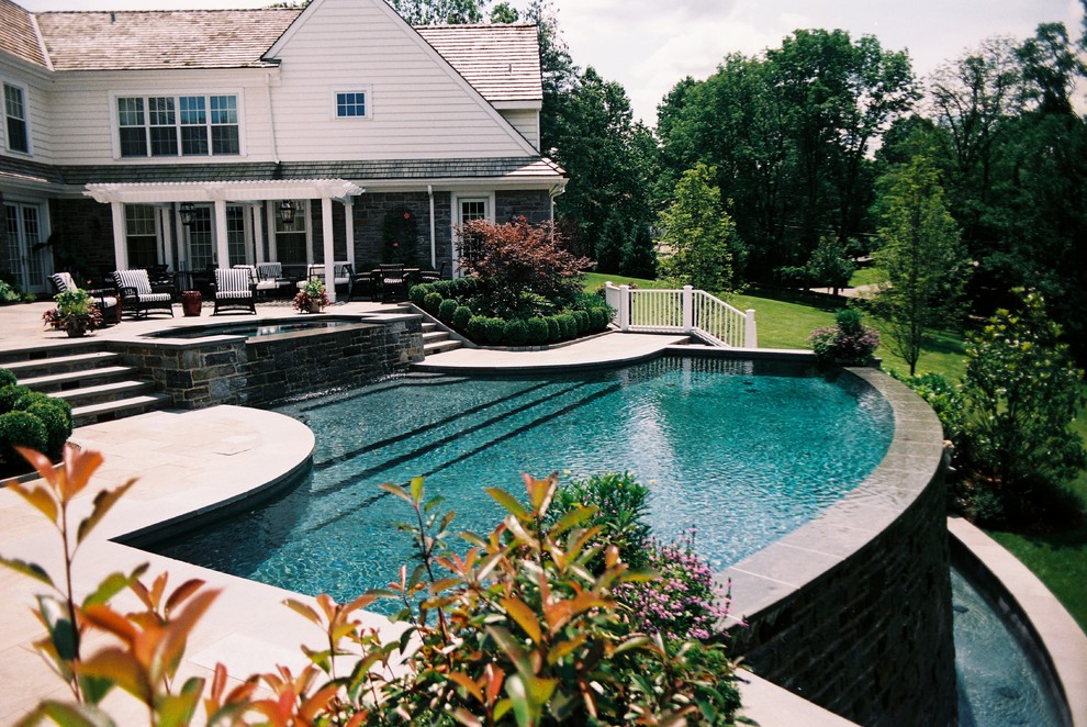 Idée de décoration pour une grande piscine à débordement et arrière tradition sur mesure avec un bain bouillonnant et des pavés en pierre naturelle.