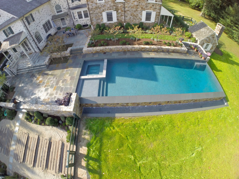 На фото: большой прямоугольный бассейн-инфинити на заднем дворе в классическом стиле с фонтаном и покрытием из каменной брусчатки
