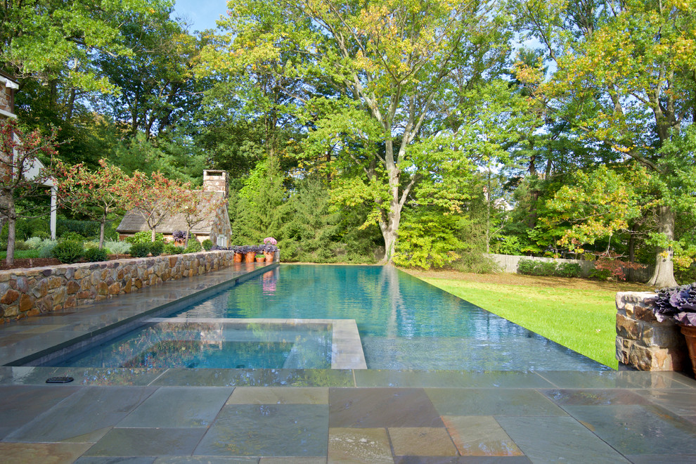 Example of a large classic backyard stone and rectangular infinity pool fountain design in Philadelphia