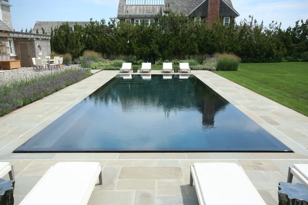 Réalisation d'une piscine à débordement et arrière design rectangle avec des pavés en pierre naturelle.