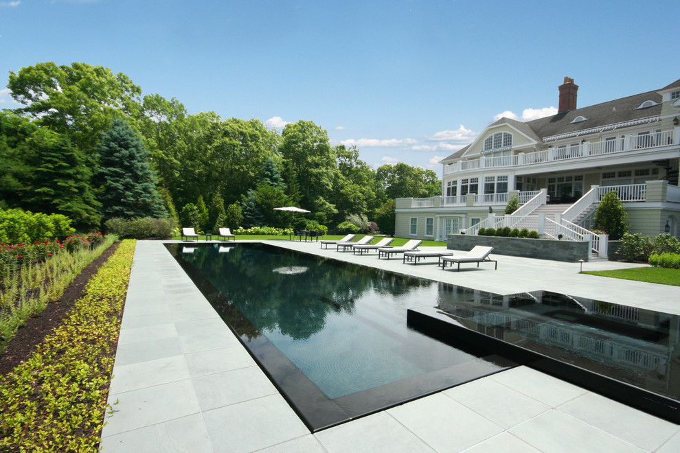 Aménagement d'une grande piscine à débordement classique rectangle avec un bain bouillonnant et des pavés en pierre naturelle.