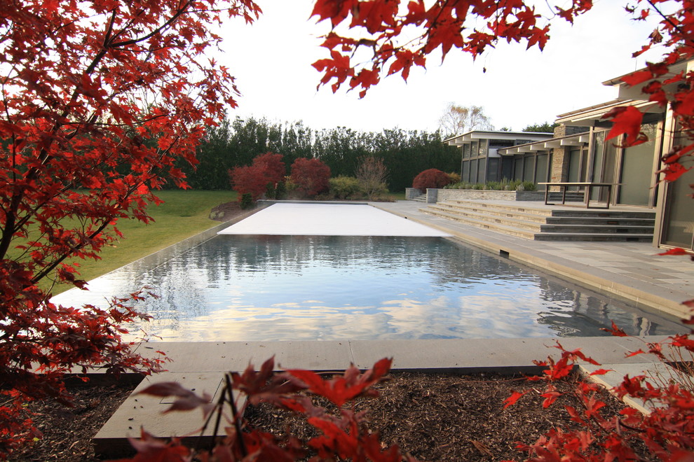 This is an example of a contemporary back rectangular infinity swimming pool in New York with natural stone paving.
