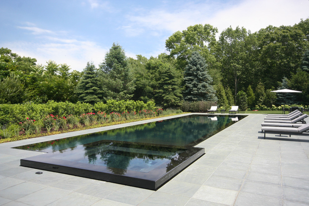 Aménagement d'une grande piscine à débordement classique rectangle avec des pavés en pierre naturelle.