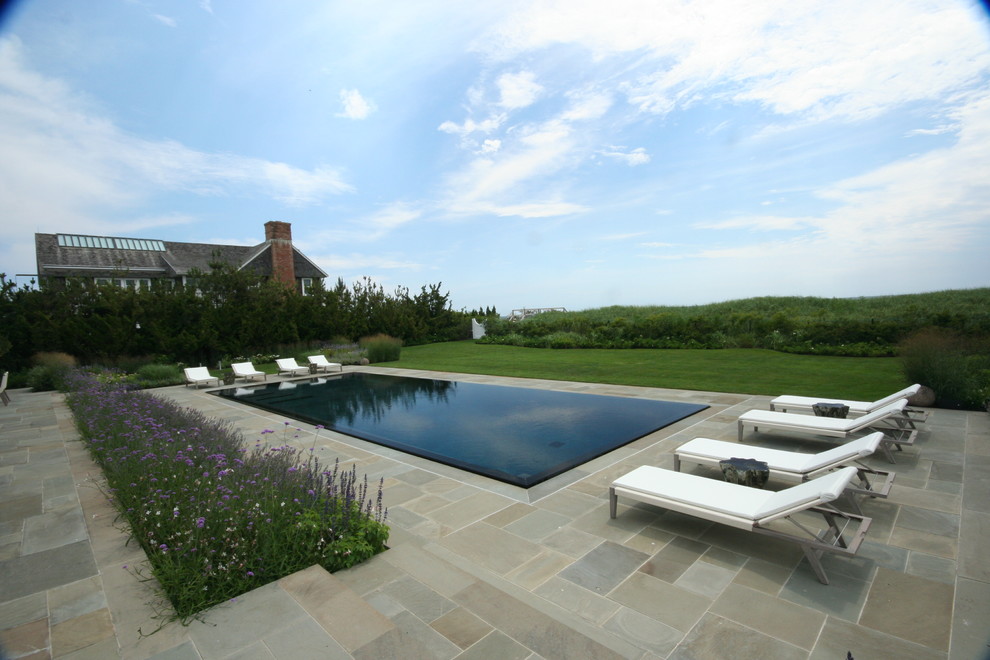 Idee per una piscina a sfioro infinito minimal rettangolare dietro casa con pavimentazioni in pietra naturale