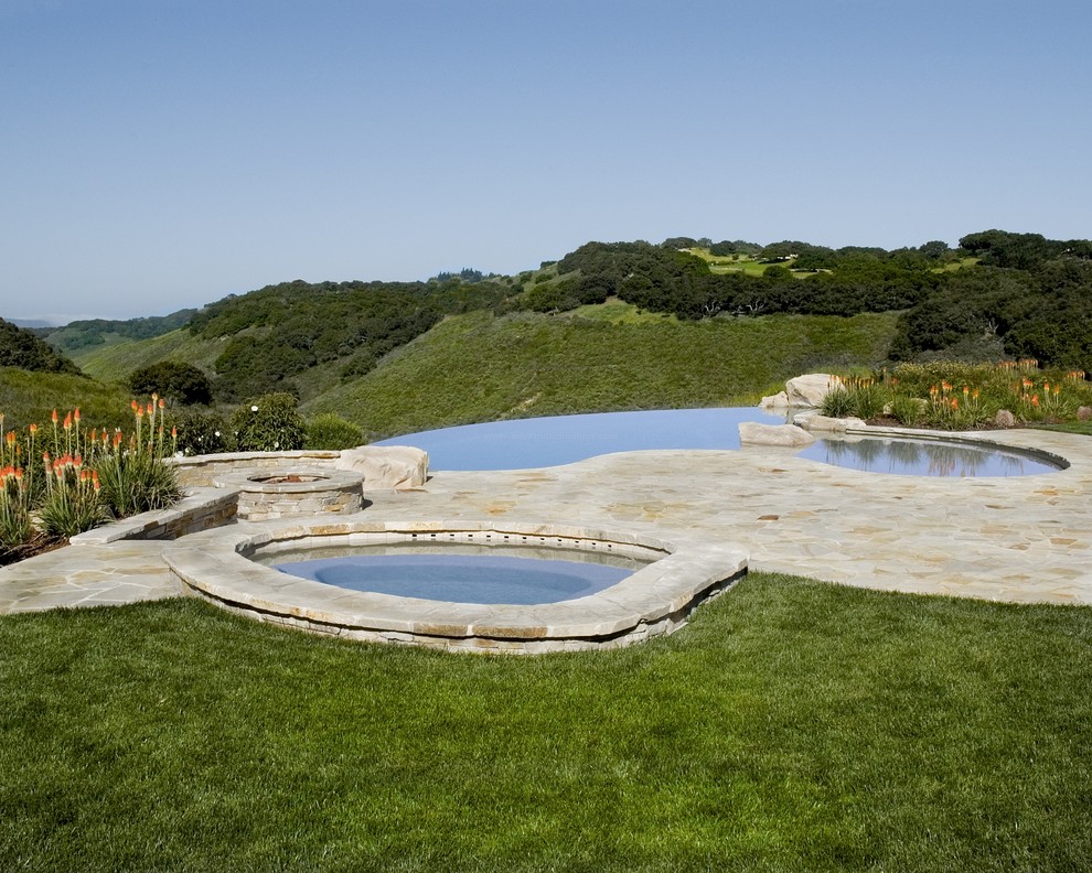 Стильный дизайн: огромный бассейн-инфинити произвольной формы на заднем дворе в средиземноморском стиле с покрытием из каменной брусчатки и джакузи - последний тренд