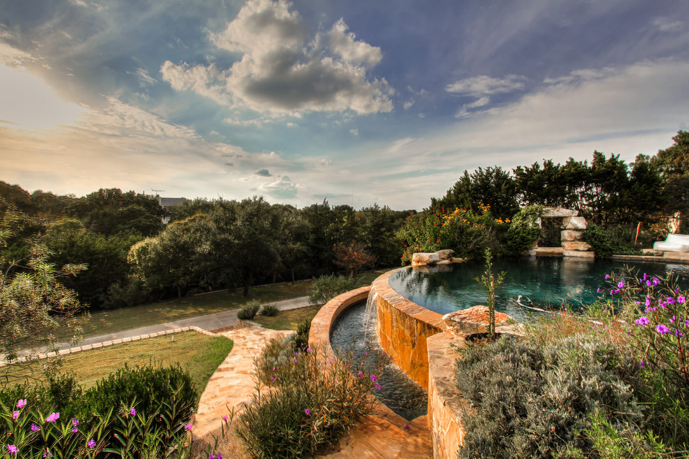 Inspiration for a large classic back custom shaped infinity swimming pool in Austin with a water feature and natural stone paving.