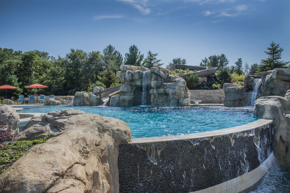 Esempio di un'ampia piscina a sfioro infinito personalizzata dietro casa con un acquascivolo e pavimentazioni in pietra naturale