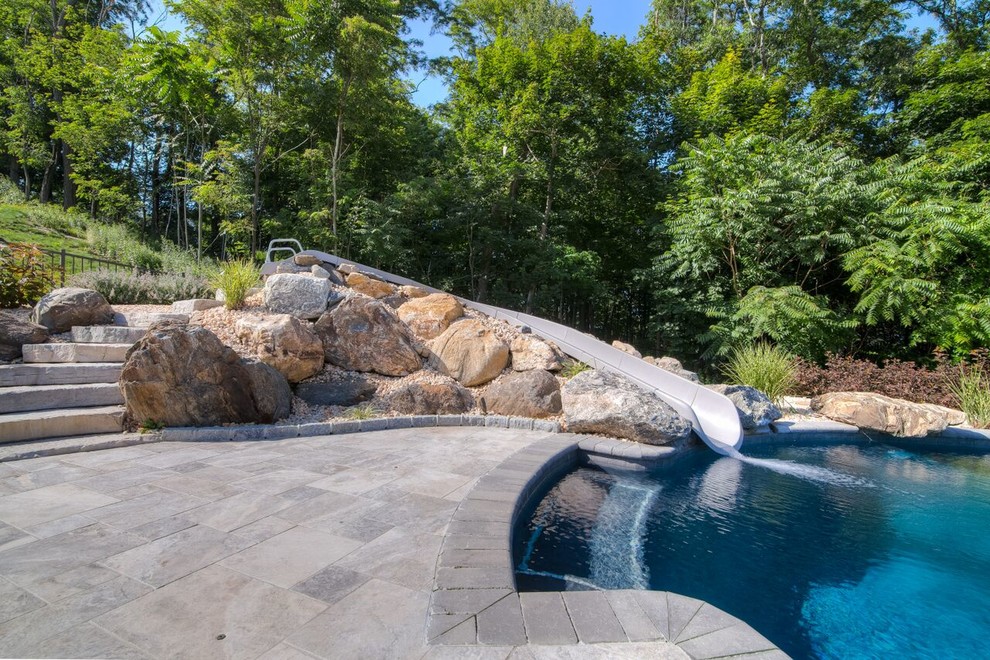 Diseño de piscina con tobogán infinita actual a medida en patio trasero con adoquines de piedra natural