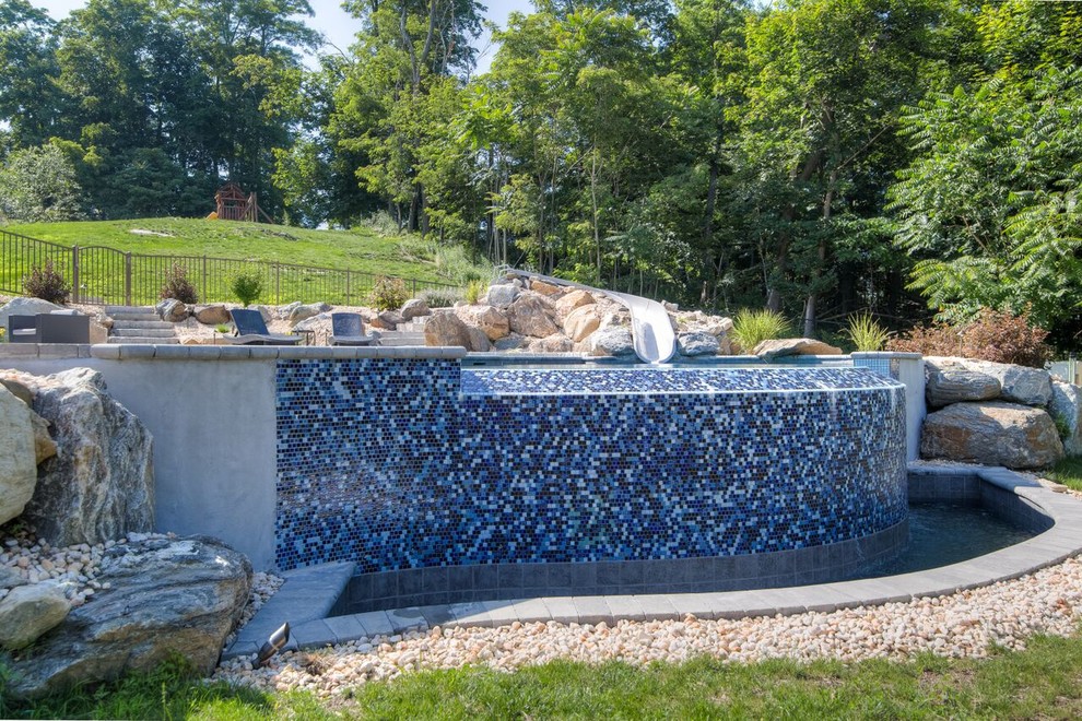 Foto de piscina con tobogán infinita actual a medida en patio trasero con adoquines de piedra natural