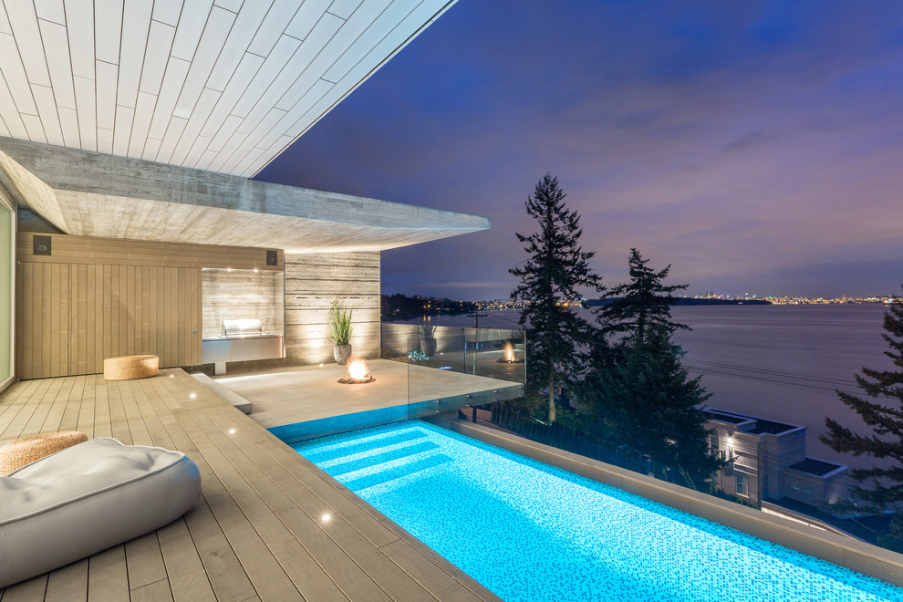 This is an example of a contemporary back rectangular infinity swimming pool in Vancouver with concrete slabs.
