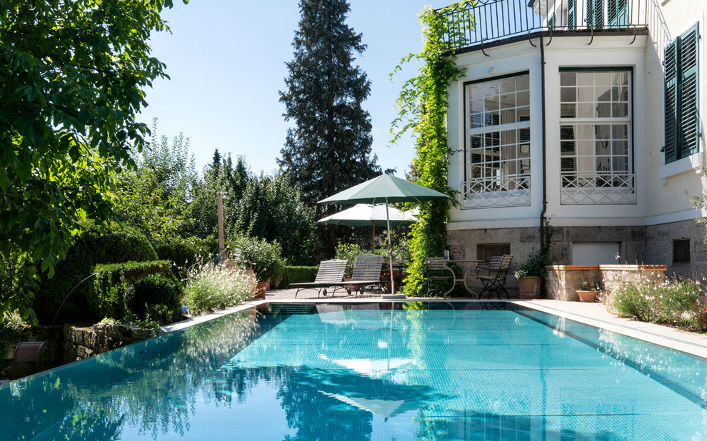 Foto de piscina infinita actual extra grande rectangular en patio lateral con suelo de baldosas