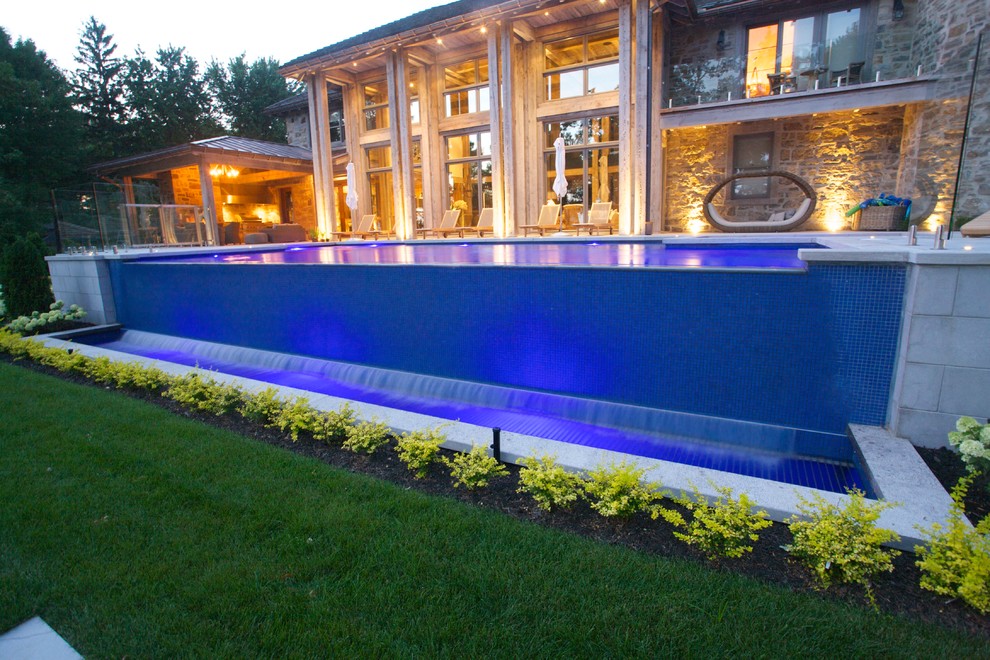 Large contemporary back rectangular infinity swimming pool in Montreal with a water feature and concrete paving.