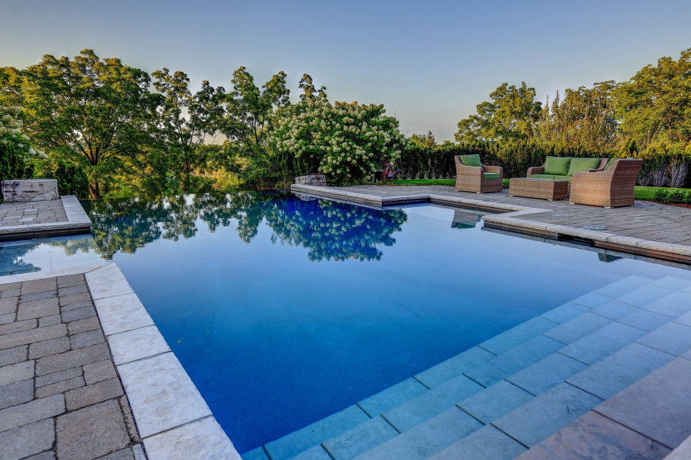Foto de piscina infinita clásica renovada de tamaño medio rectangular en patio trasero con adoquines de hormigón