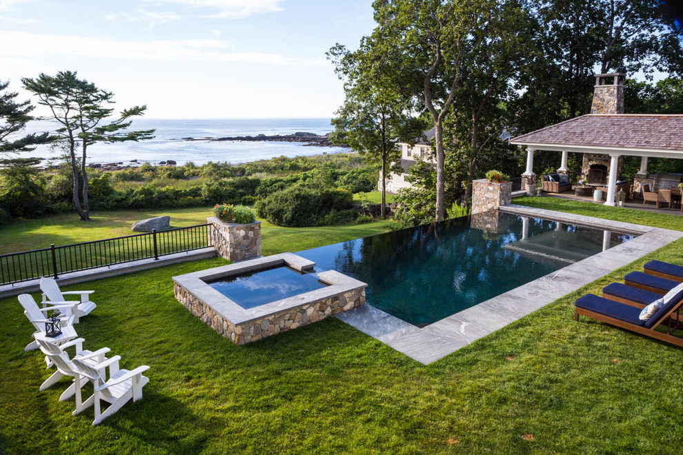 Example of a mid-sized classic backyard rectangular and stone infinity hot tub design in Portland Maine