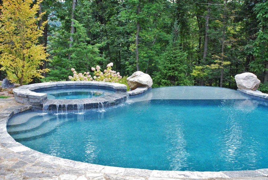 Exemple d'une grande piscine à débordement et arrière moderne sur mesure avec un bain bouillonnant et du béton estampé.