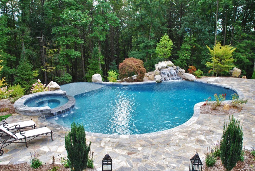 Idée de décoration pour une grande piscine à débordement et arrière minimaliste sur mesure avec un bain bouillonnant et du béton estampé.