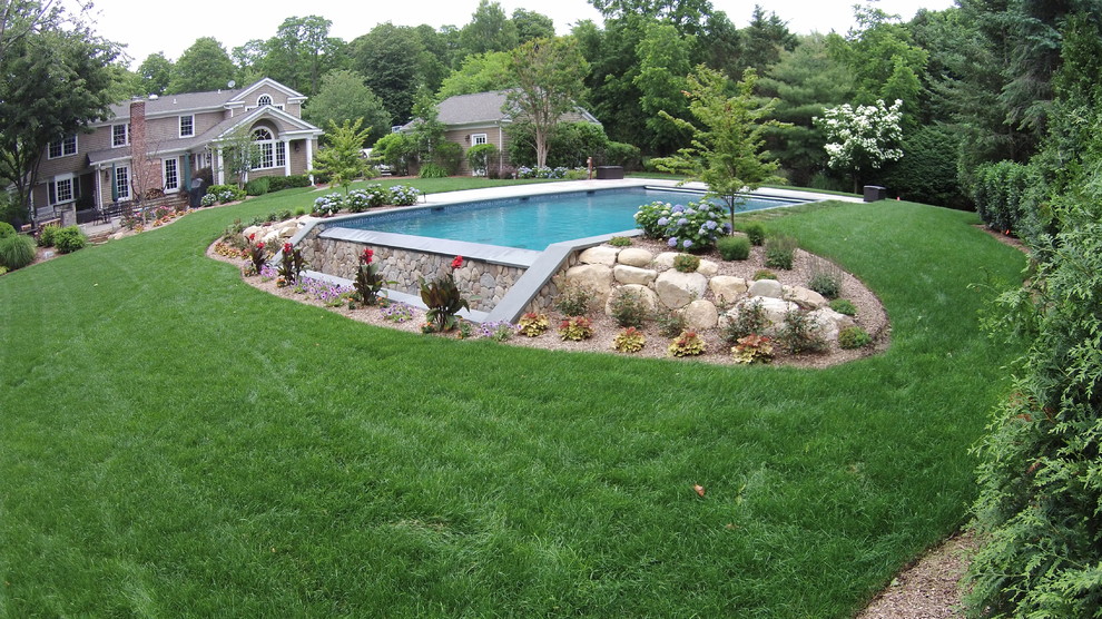 На фото: большой прямоугольный бассейн-инфинити на заднем дворе в стиле неоклассика (современная классика) с фонтаном и покрытием из каменной брусчатки