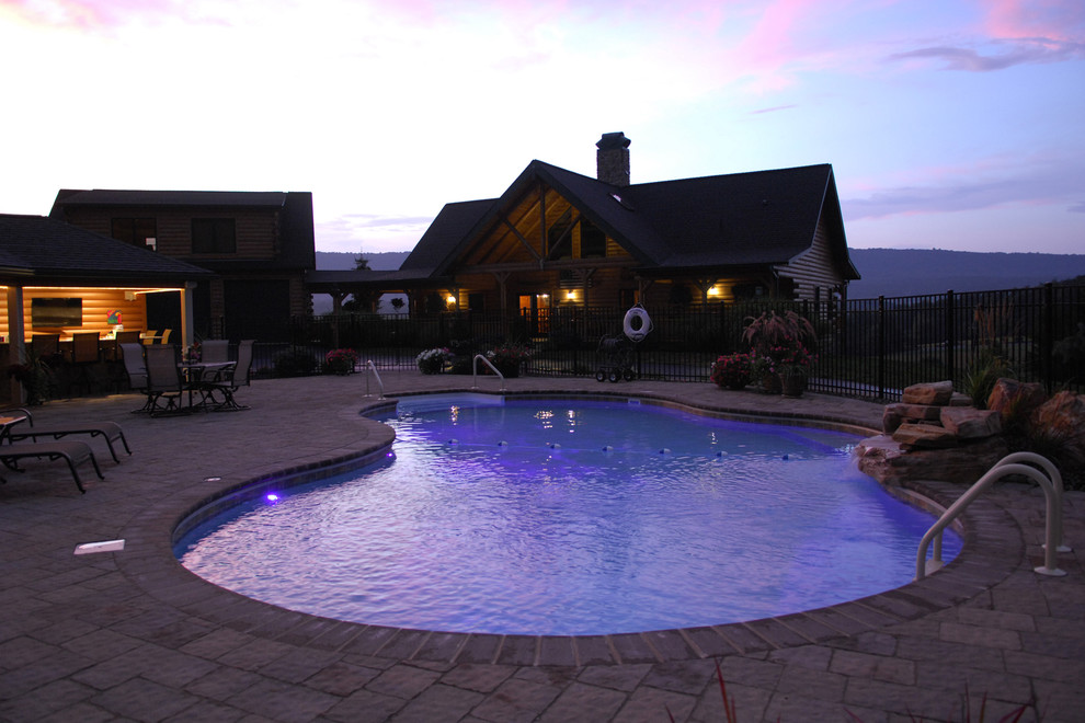 Ejemplo de piscina alargada clásica grande tipo riñón en patio trasero con adoquines de hormigón