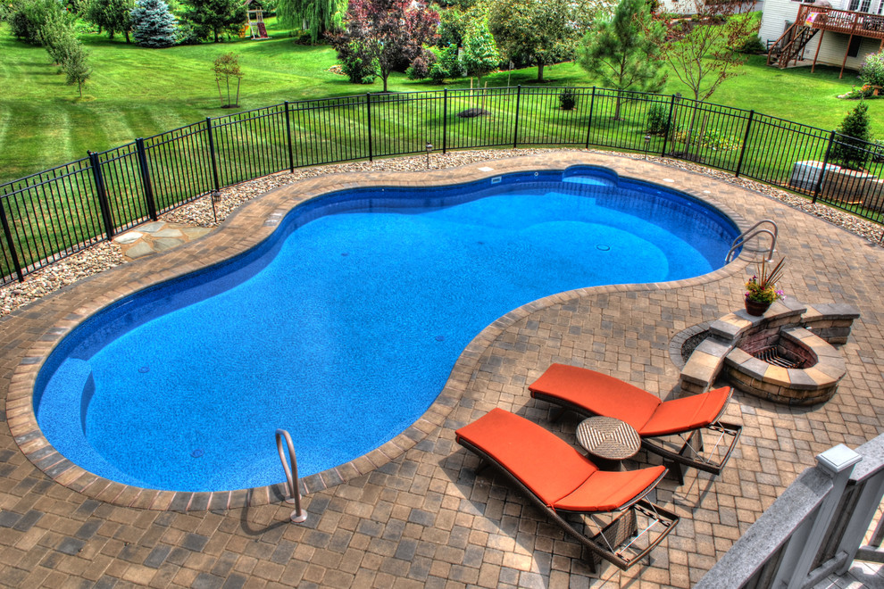 Foto de piscina alargada clásica grande tipo riñón en patio trasero con adoquines de hormigón