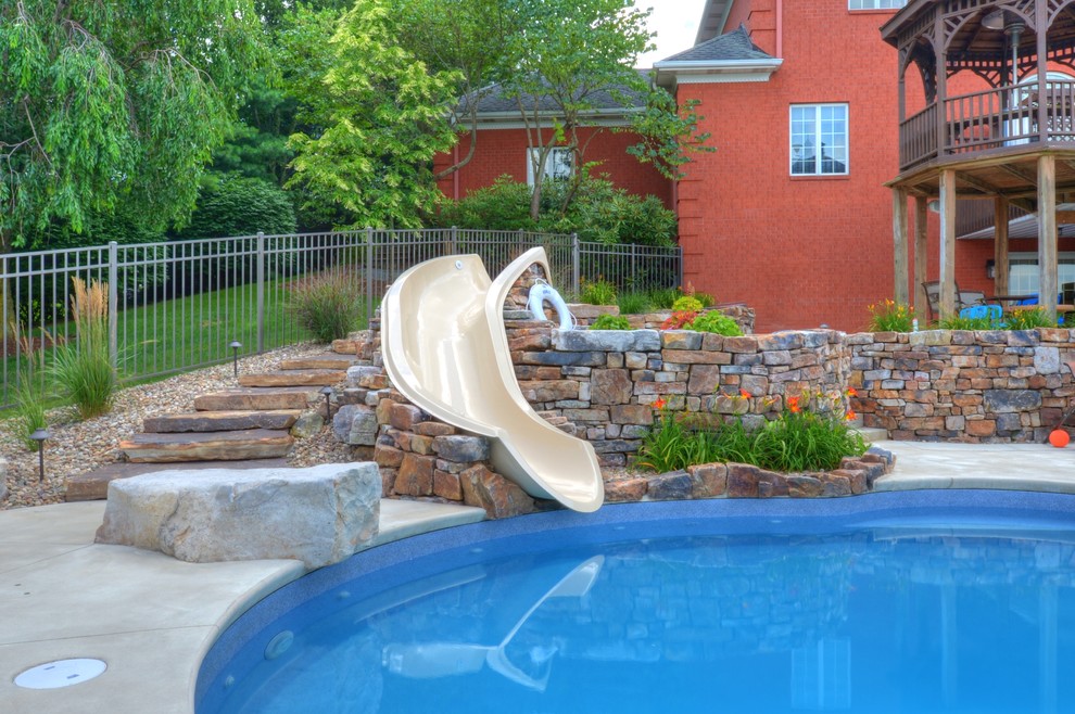 На фото: большой спортивный бассейн в форме фасоли на заднем дворе в классическом стиле с водной горкой и покрытием из бетонных плит