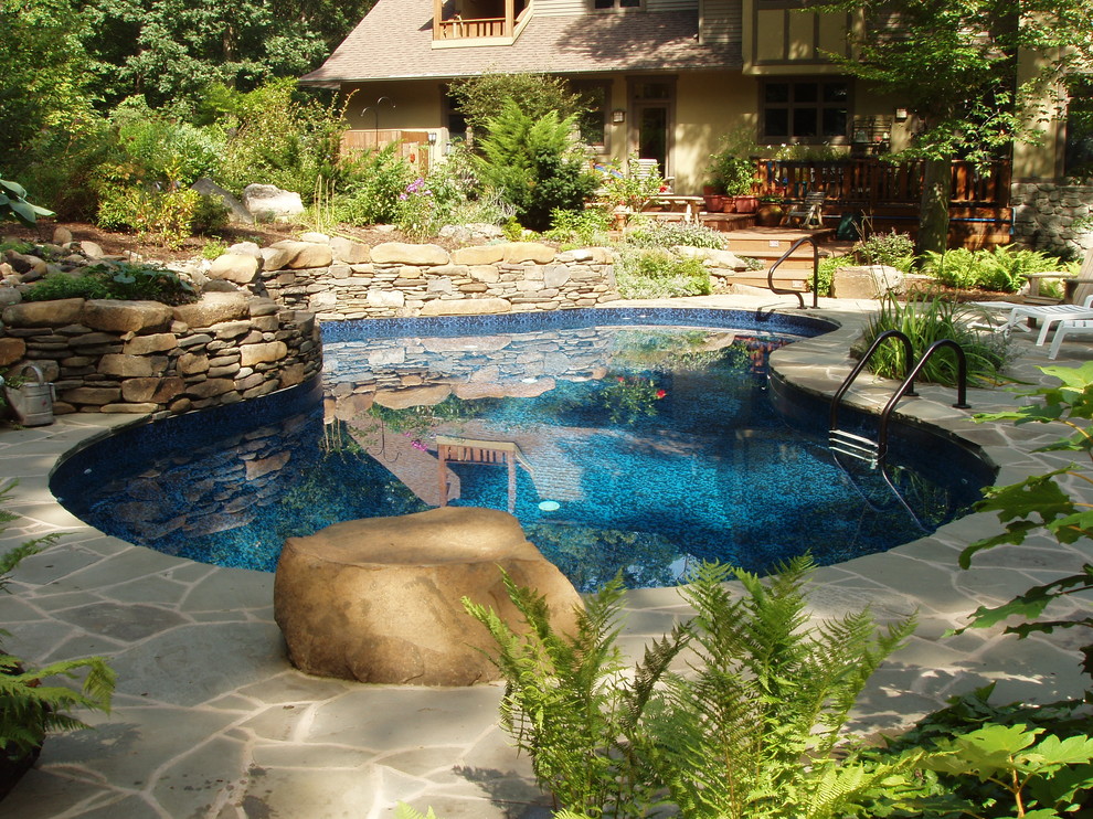 Modelo de piscina ecléctica de tamaño medio a medida en patio trasero con adoquines de piedra natural