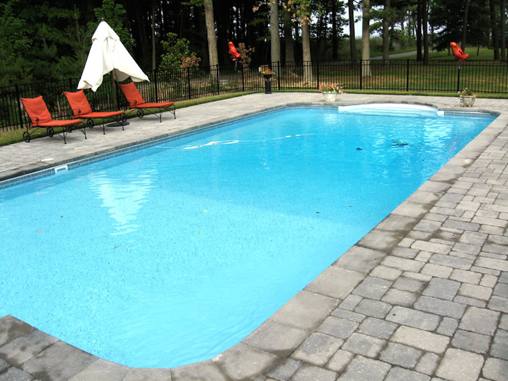 Modelo de piscina alargada minimalista grande rectangular en patio trasero con adoquines de ladrillo