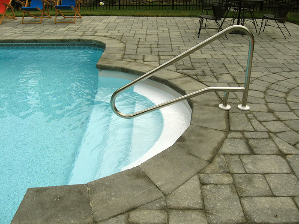 Diseño de piscina alargada moderna grande rectangular en patio trasero con adoquines de ladrillo