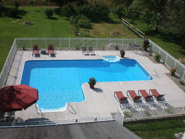 Diseño de piscina alargada tradicional grande en forma de L en patio trasero con losas de hormigón