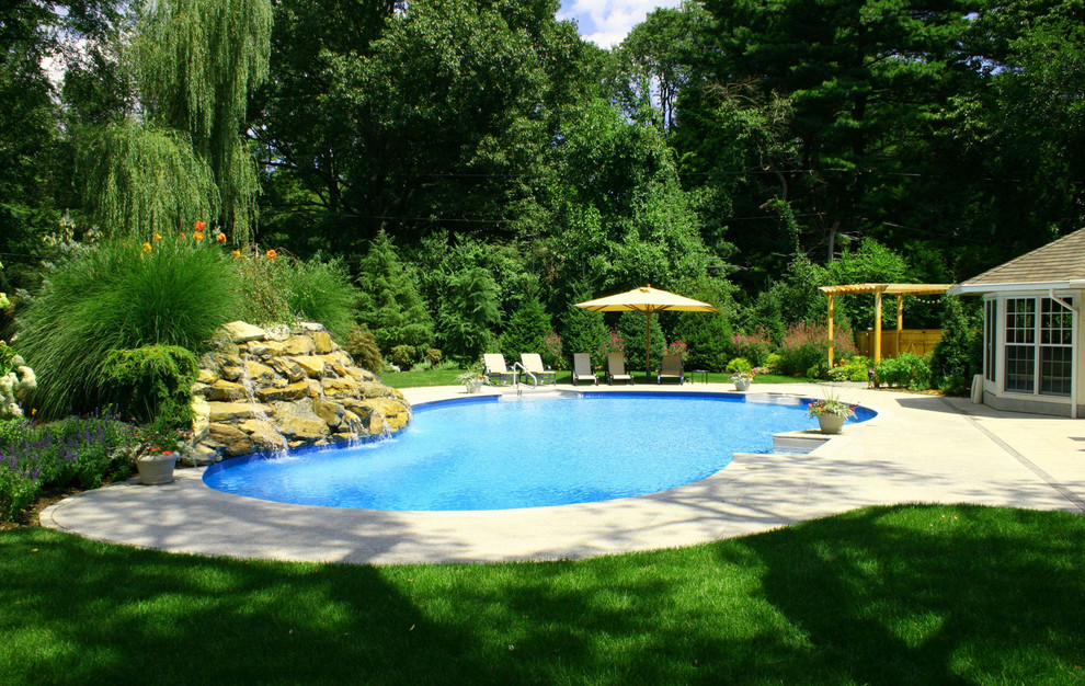 Klassisk inredning av en stor anpassad pool på baksidan av huset, med betongplatta