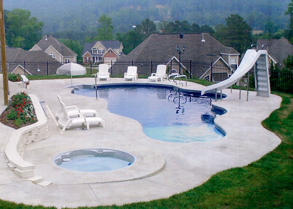 Immagine di una grande piscina naturale tradizionale personalizzata dietro casa con lastre di cemento e un acquascivolo