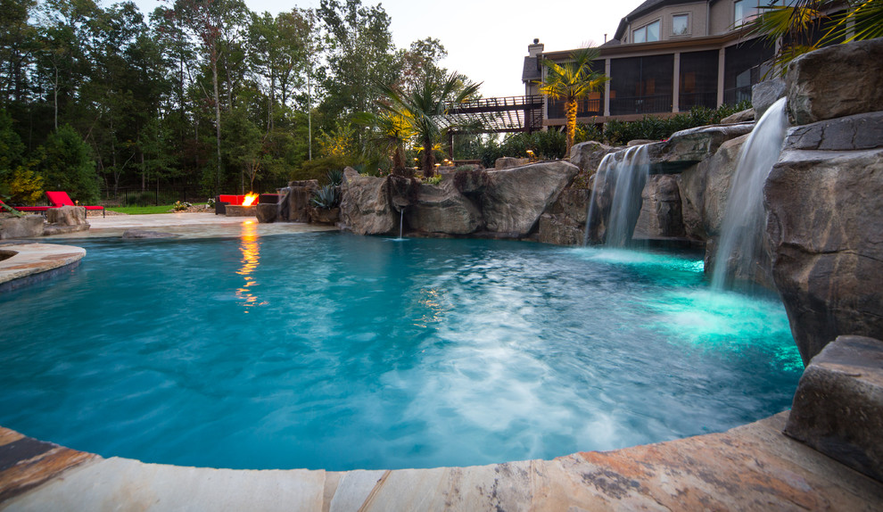 Pool fountain - large tropical backyard stone and custom-shaped pool fountain idea in Charlotte