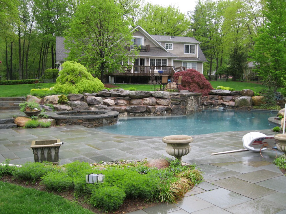 Photo of a large traditional back custom shaped natural swimming pool in New York with a water feature and natural stone paving.