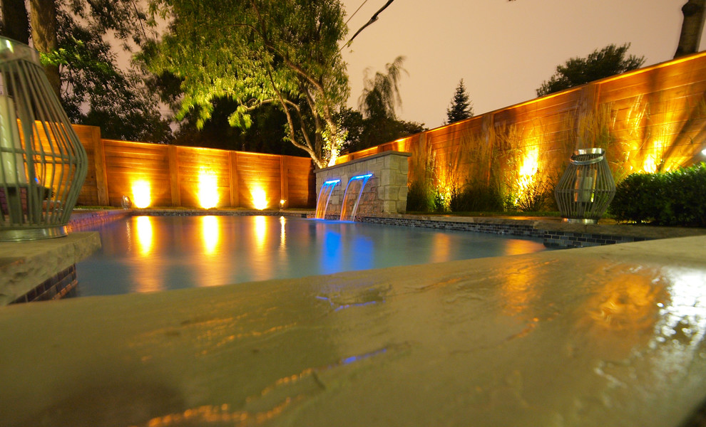 Modelo de piscina con fuente natural moderna de tamaño medio rectangular en patio trasero con adoquines de hormigón