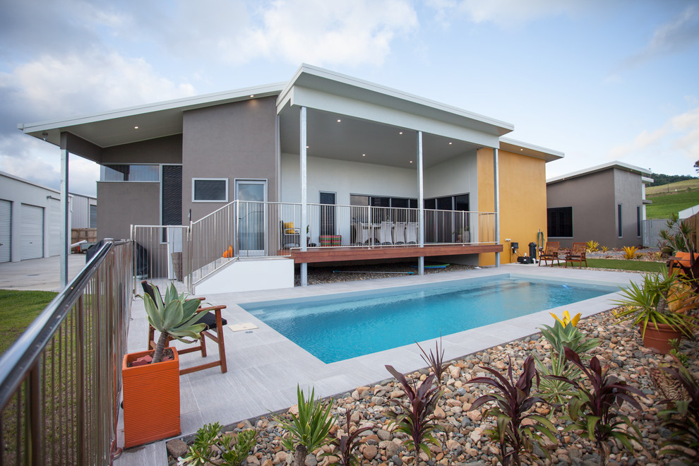 Diseño de piscina alargada contemporánea de tamaño medio rectangular en patio trasero con paisajismo de piscina y suelo de baldosas