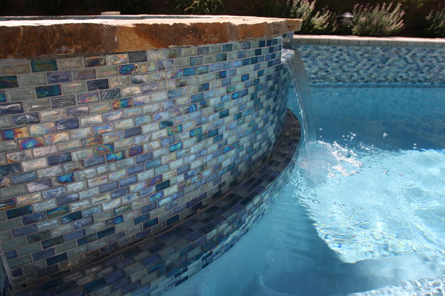 Iridescent blue 1” X 2” glass tile surrounds the pool and raised spa ...