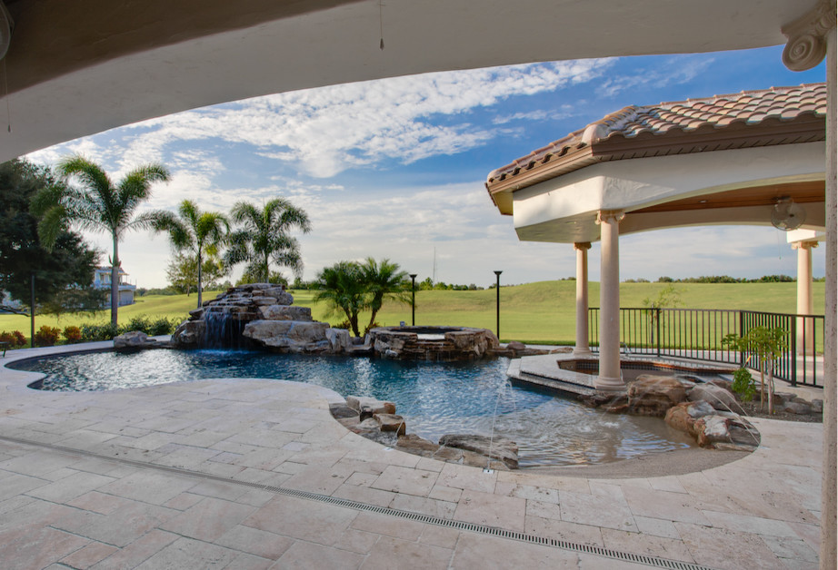 Diseño de piscina exótica grande a medida en patio trasero con adoquines de piedra natural