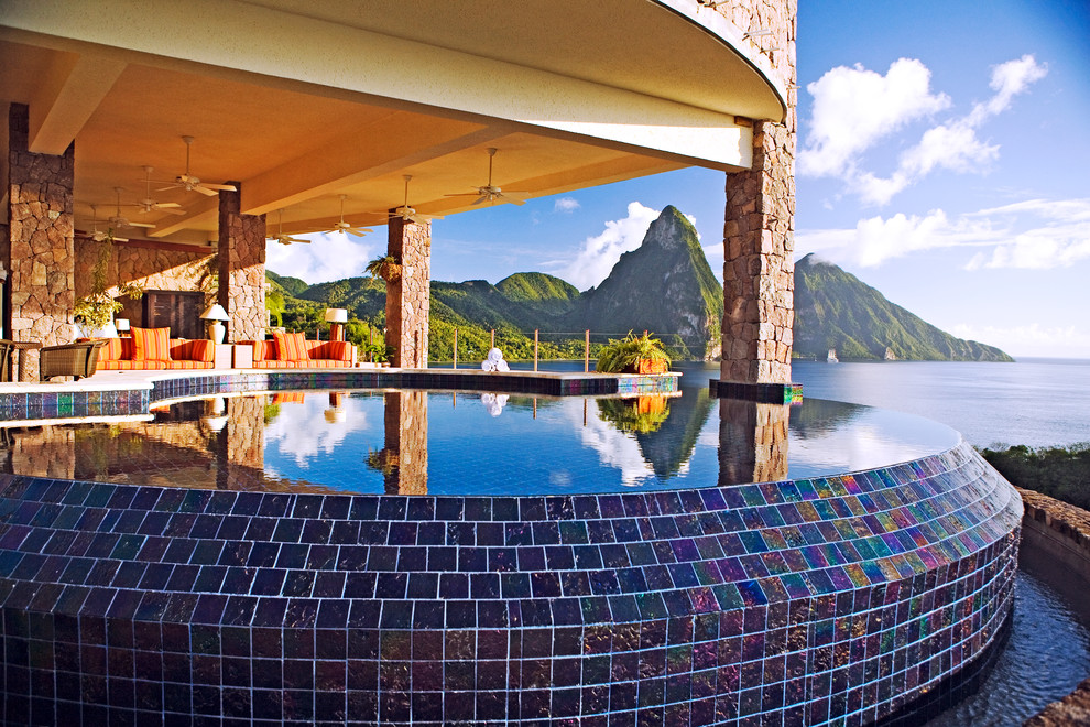 Immagine di un'ampia piscina a sfioro infinito tropicale personalizzata con una dépendance a bordo piscina e piastrelle