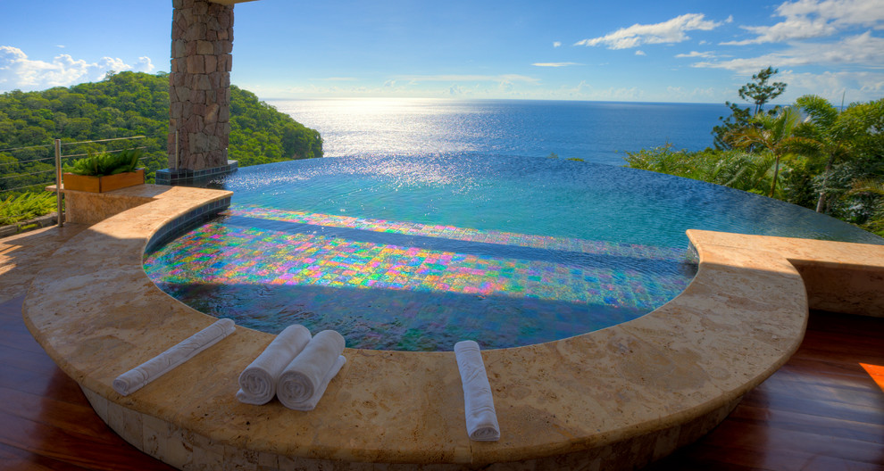 Immagine di un'ampia piscina a sfioro infinito tropicale personalizzata sul tetto con fontane e piastrelle