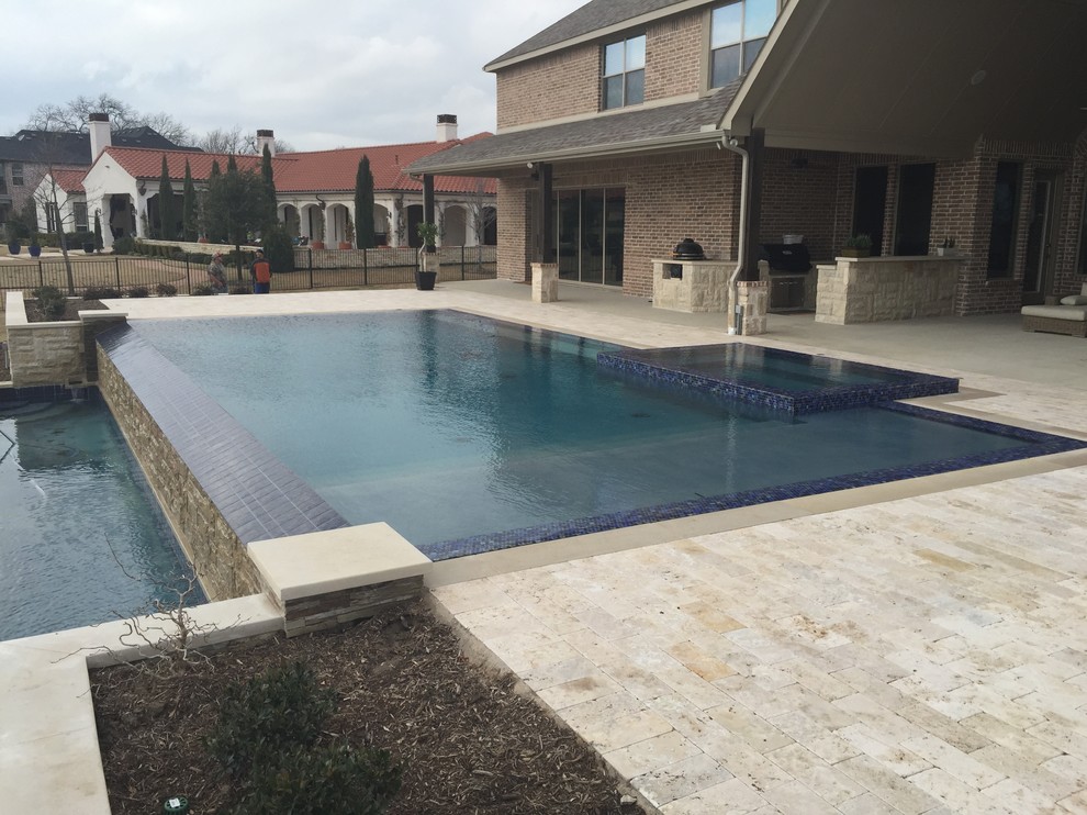 Esempio di una grande piscina a sfioro infinito minimalista rettangolare dietro casa con pavimentazioni in pietra naturale e una vasca idromassaggio