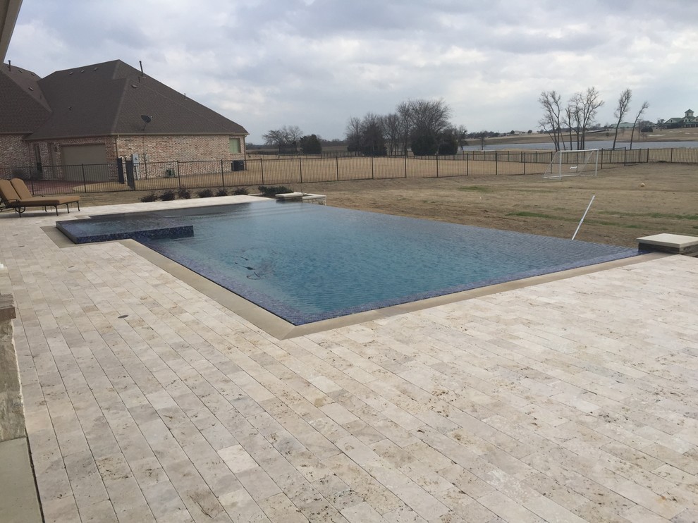 На фото: большой прямоугольный бассейн-инфинити на заднем дворе в стиле модернизм с покрытием из каменной брусчатки и джакузи